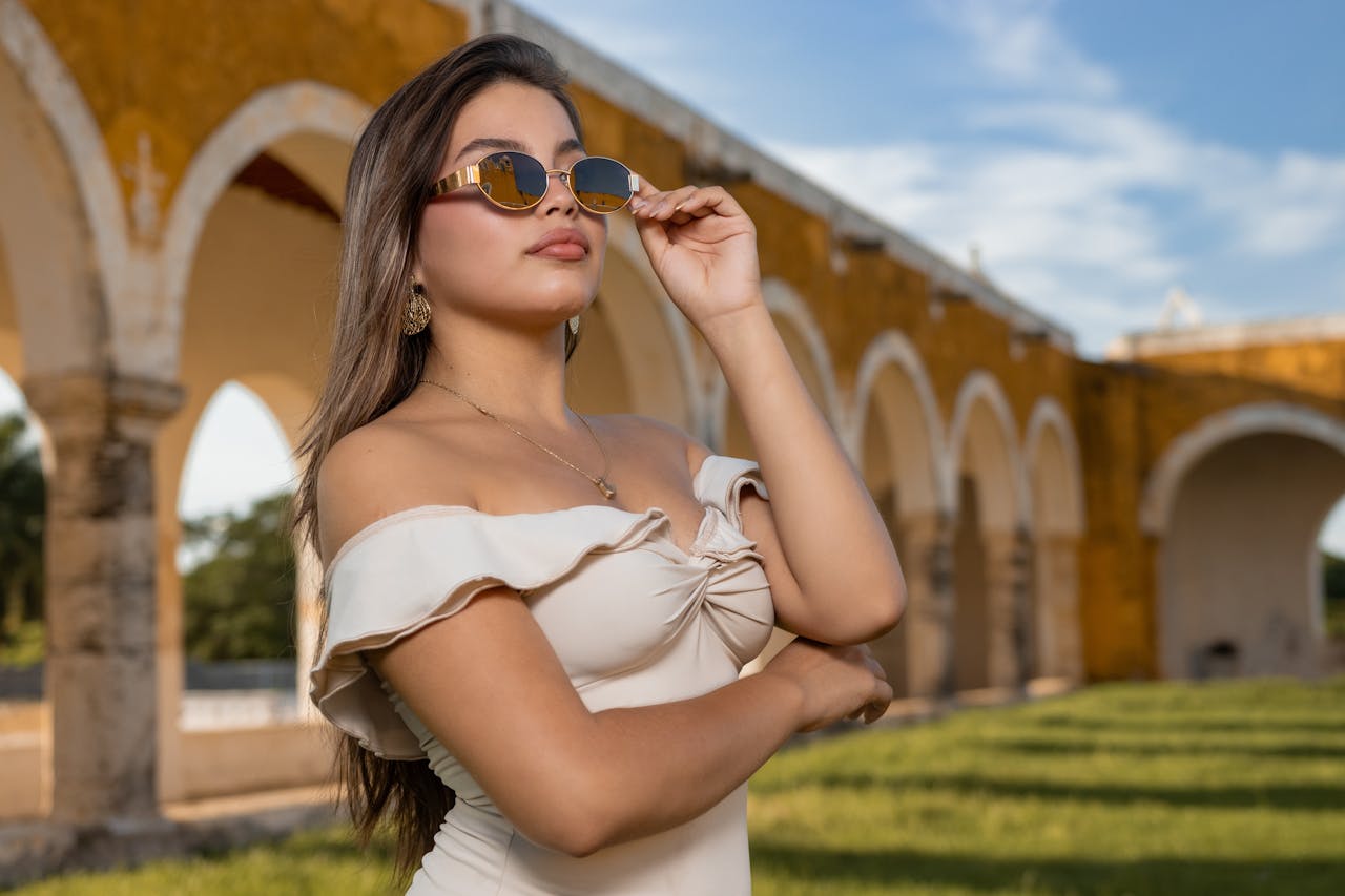 Woman in off-shoulder dress poses with sunglasses at a historical site with arches.